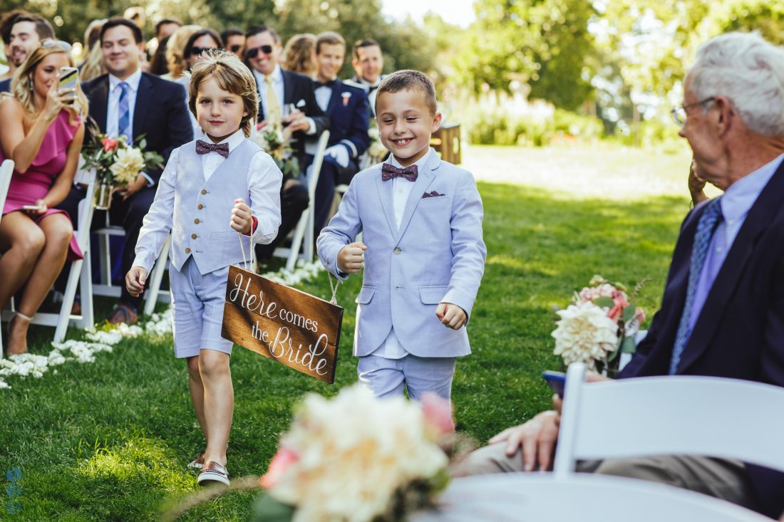 Ring bearers carrying the here comes the bride sign into the wedding ceremony.