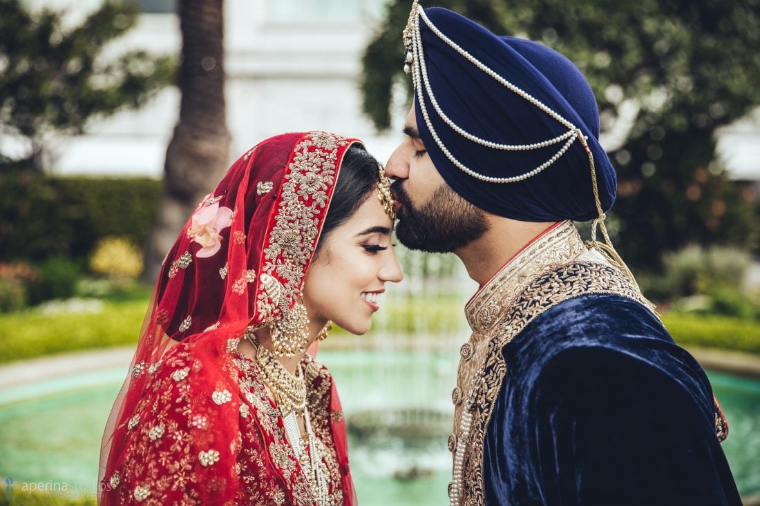 Indian bride in red lehenga and groom kiss in a rooftop garden at Fairmont San Francisco
