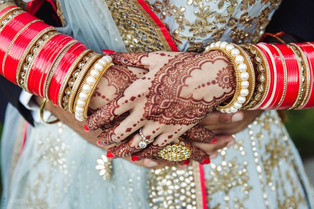 Indian bride in Pratap Sons wedding dress, gold jewelry, red bangles, henna mehndi art